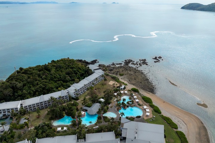 Aerial view of beachfront resort with pools, greenery, and ocean.