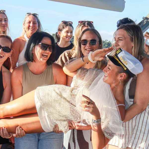 Group of smiling women holding a woman in a captain's hat on a boat.